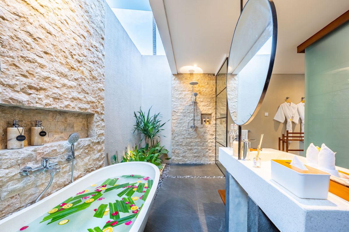 Modern wooden kitchen and dining area with set table, tropical flowers, and sliding glass doors to a lush balcony. - Bali Villas