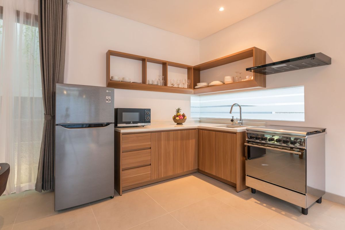 Modern wooden kitchen and dining area with set table, tropical flowers, and sliding glass doors to a lush balcony. - Bali Villas