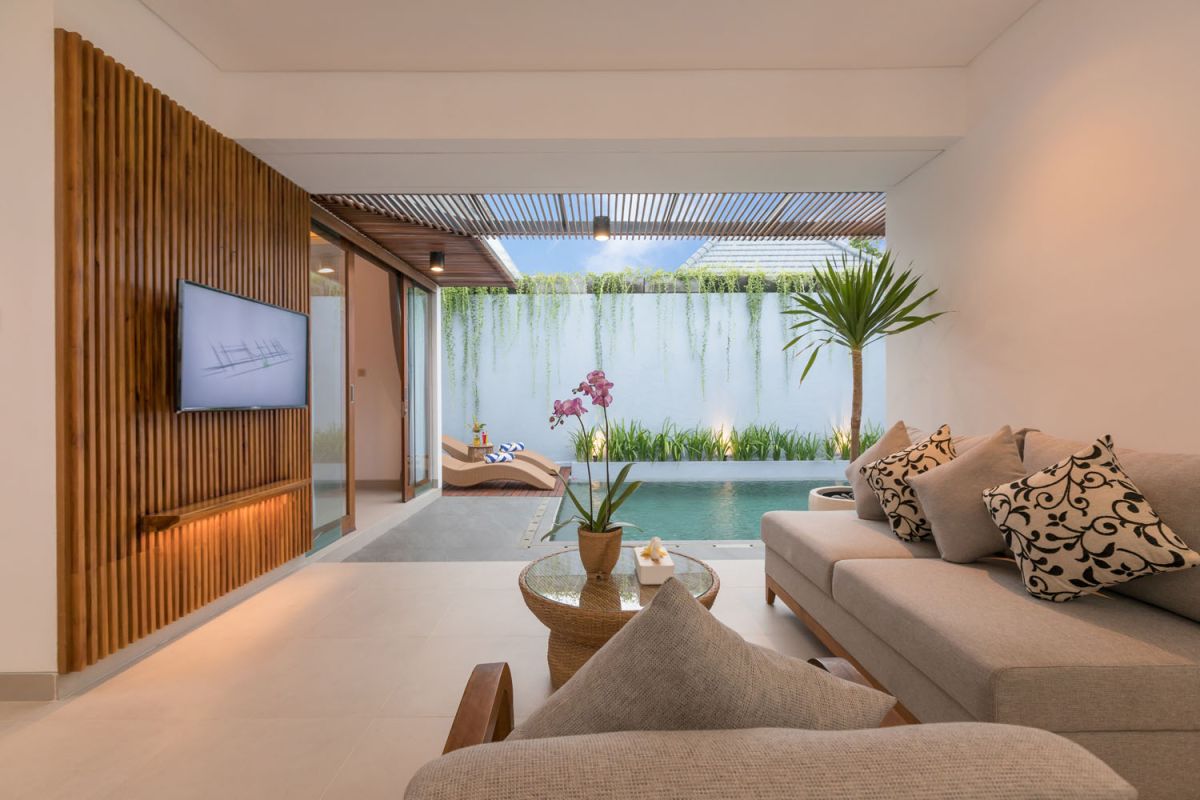 Modern wooden kitchen and dining area with set table, tropical flowers, and sliding glass doors to a lush balcony. - Bali Villas