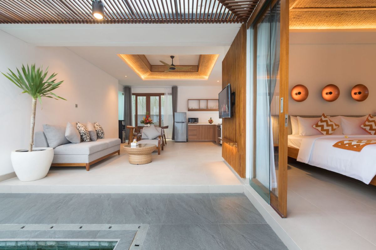 Modern tropical Bali villa interior with neutral-toned sofas, wooden dining set, potted orchids, and infinity pool view through glass doors. - Bali Villas
