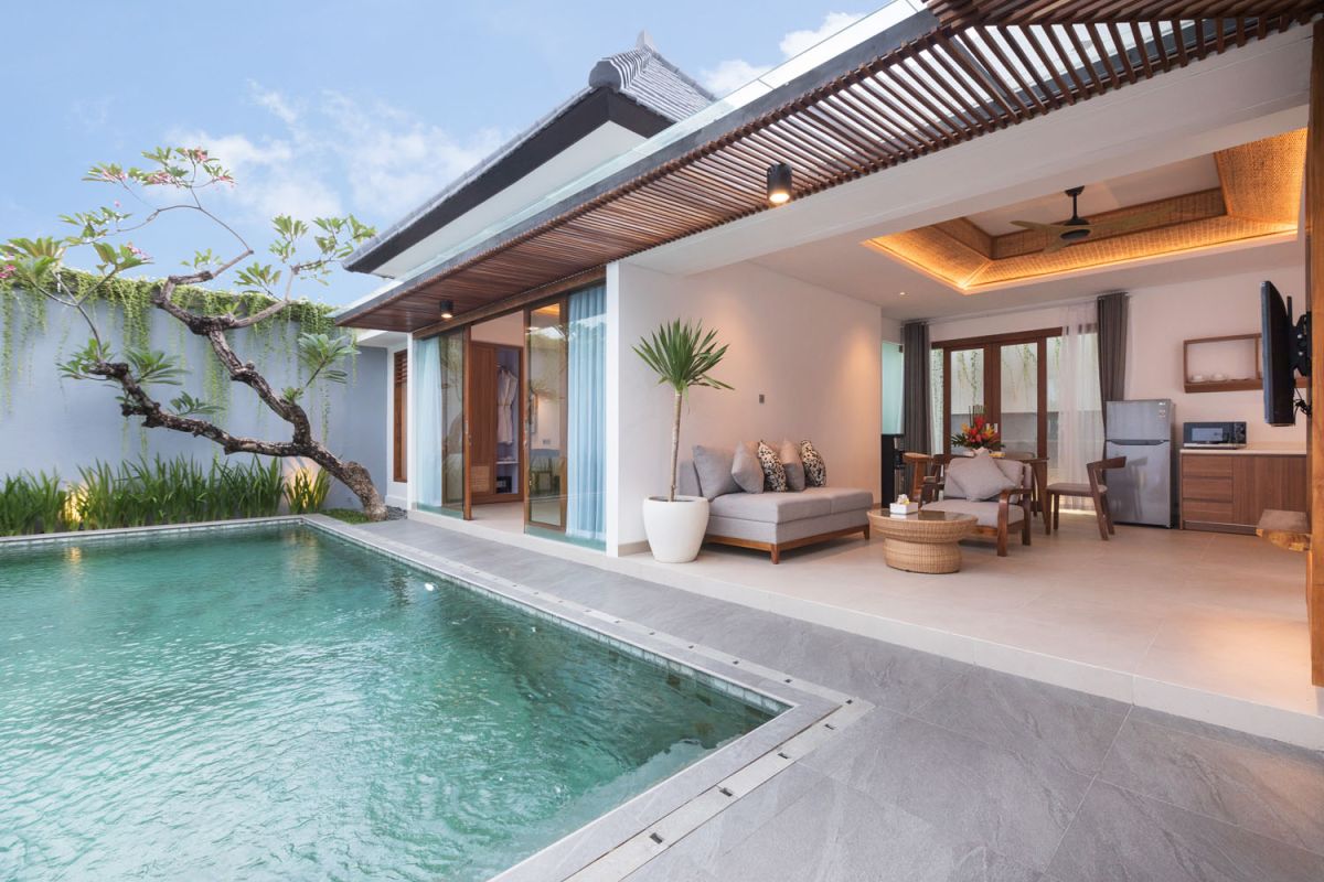Modern tropical Bali villa interior with neutral-toned sofas, wooden dining set, potted orchids, and infinity pool view through glass doors. - Bali Villas
