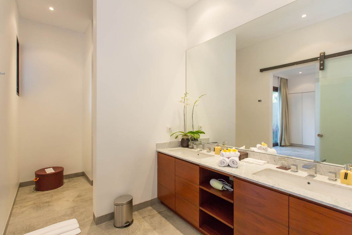 Modern luxury bathroom with wooden double vanity, white marble countertop, orchids, and folded towels. - Bali Villas