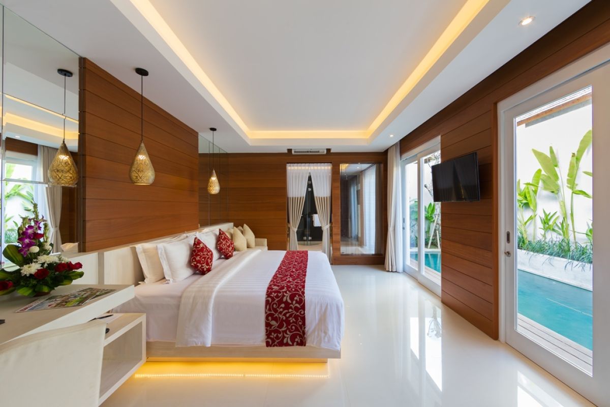 Luxurious Balinese bedroom with king bed, red accents, wooden walls, and sliding doors to a private pool with tropical greenery. - Bali Villas