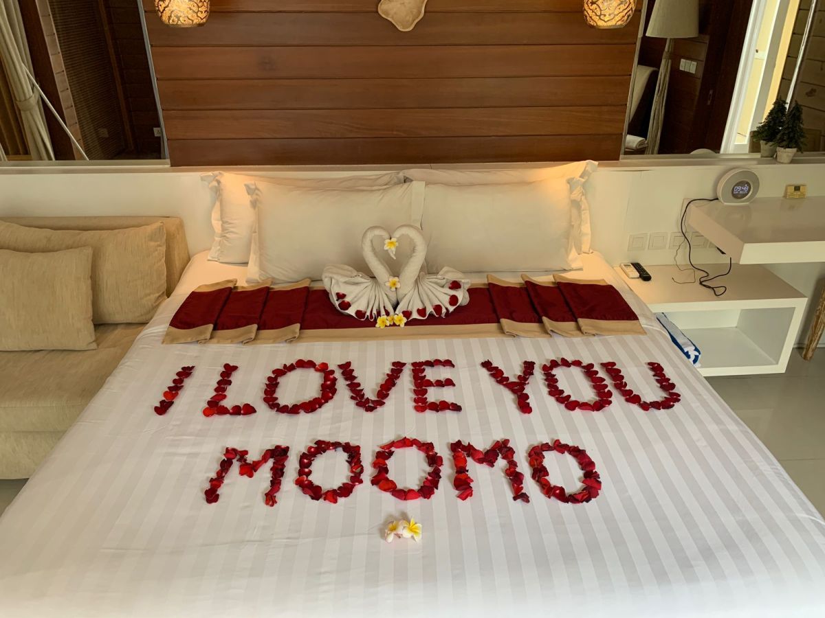Spacious Balinese villa bedroom with wooden walls, white king bed, red accents, and sliding doors to a private infinity pool. - Bali Villas