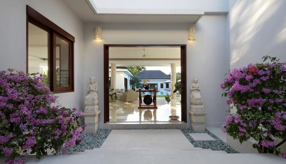 Modern tropical villa with infinity pool, purple loungers, and lush gardens under a clear blue sky. - Bali Villas