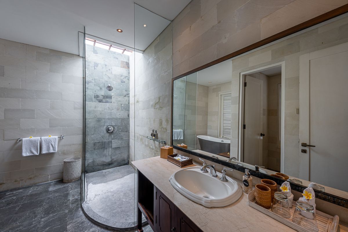 Elegant Balinese dining room with a set wooden table, rattan chairs, tropical floral centerpiece, hanging leaf lamps, and open doors to an outdoor pool. - Bali Villas