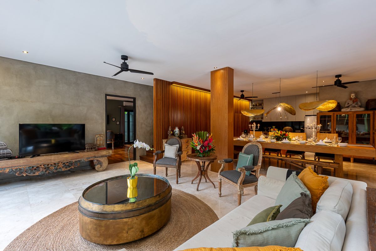 Elegant Balinese dining room with a set wooden table, rattan chairs, tropical floral centerpiece, hanging leaf lamps, and open doors to an outdoor pool. - Bali Villas