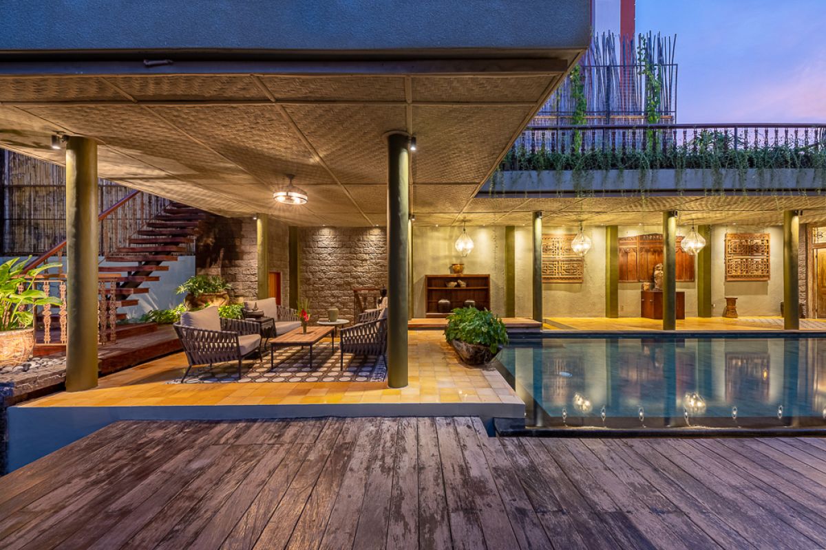 Elegant Balinese dining room with a set wooden table, rattan chairs, tropical floral centerpiece, hanging leaf lamps, and open doors to an outdoor pool. - Bali Villas