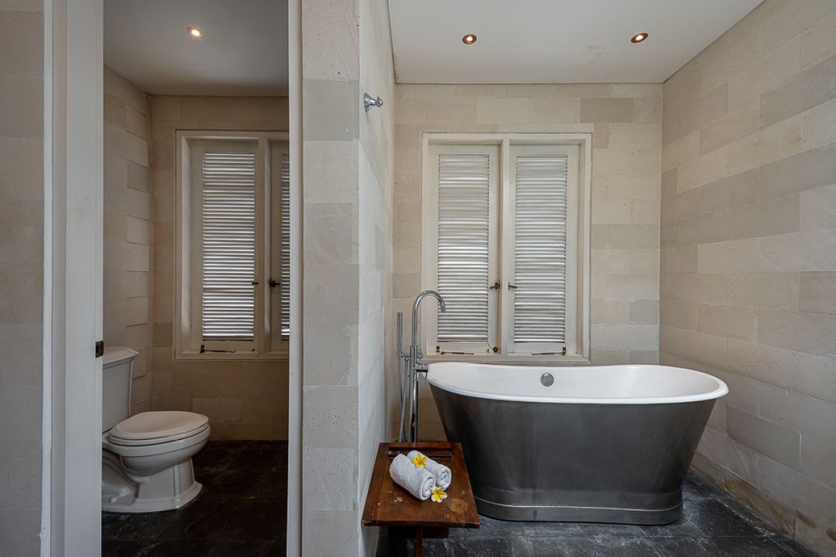 Elegant Balinese dining room with a set wooden table, rattan chairs, tropical floral centerpiece, hanging leaf lamps, and open doors to an outdoor pool. - Bali Villas