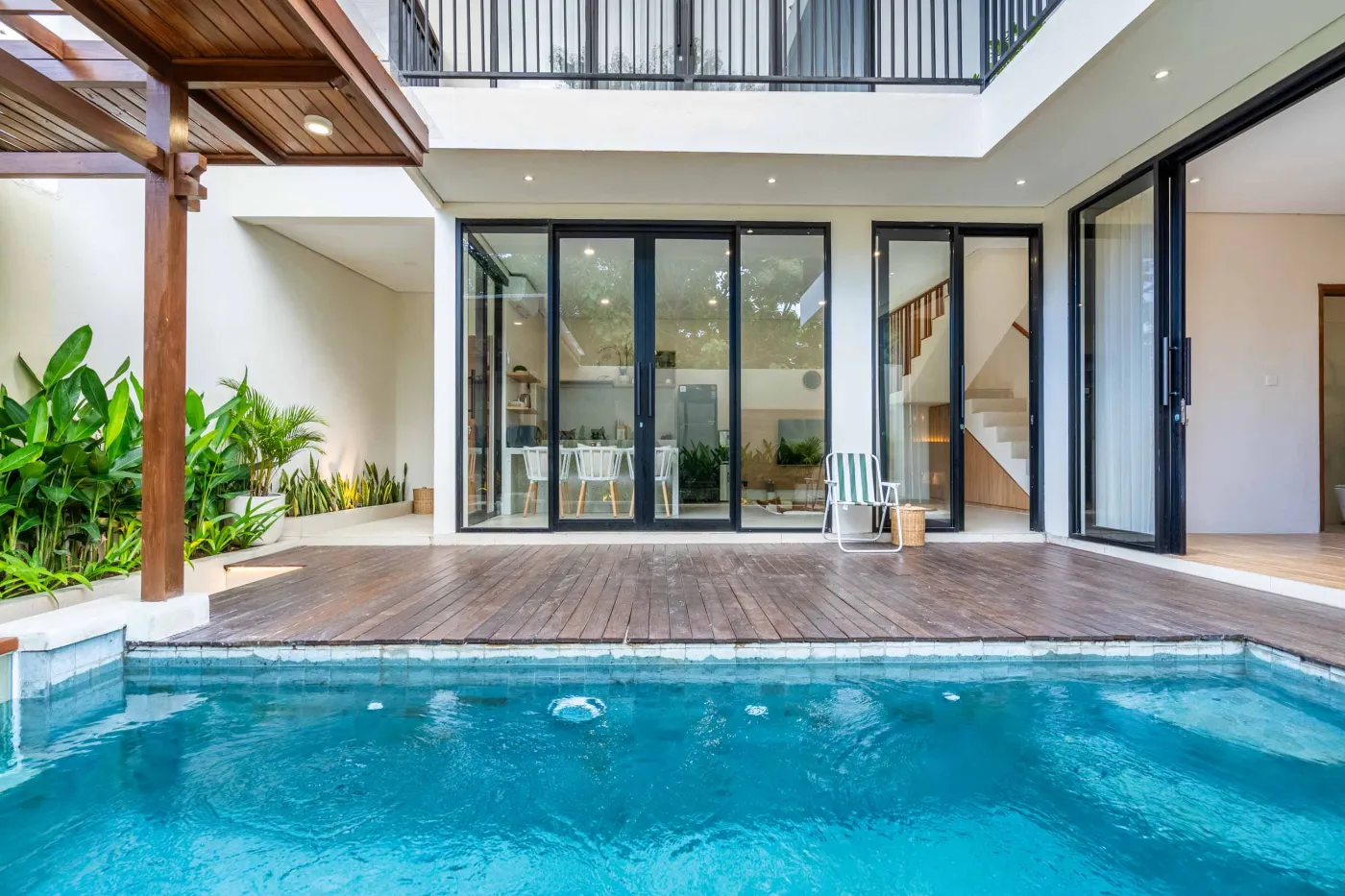 Modern minimalist bathroom featuring a freestanding white bathtub, sleek vanity sink with black faucet, round wooden mirror, and tropical plant-filled window. - Bali Villas
