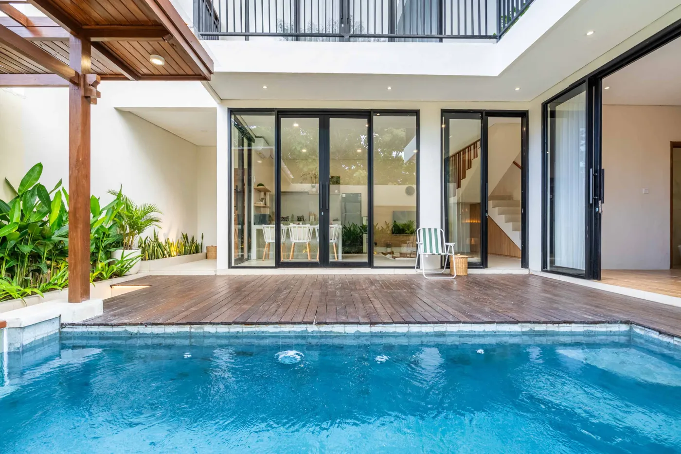 Modern minimalist bathroom featuring a freestanding white bathtub, sleek vanity sink with black faucet, round wooden mirror, and tropical plant-filled window. - Bali Villas