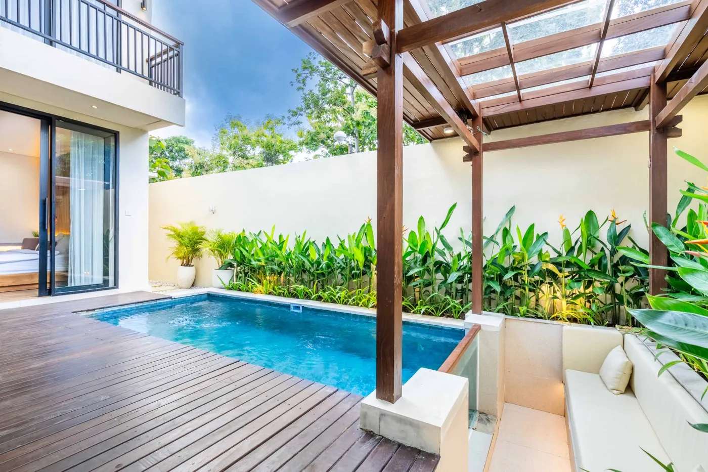 Modern minimalist bathroom featuring a freestanding white bathtub, sleek vanity sink with black faucet, round wooden mirror, and tropical plant-filled window. - Bali Villas