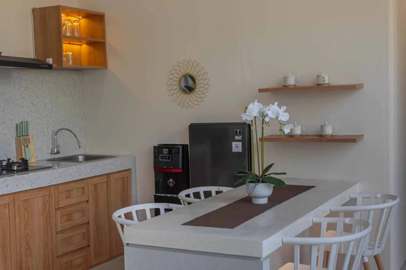 Modern minimalist kitchen with wooden cabinets, white orchids on a central table, fridge, and sink. - Bali Villas
