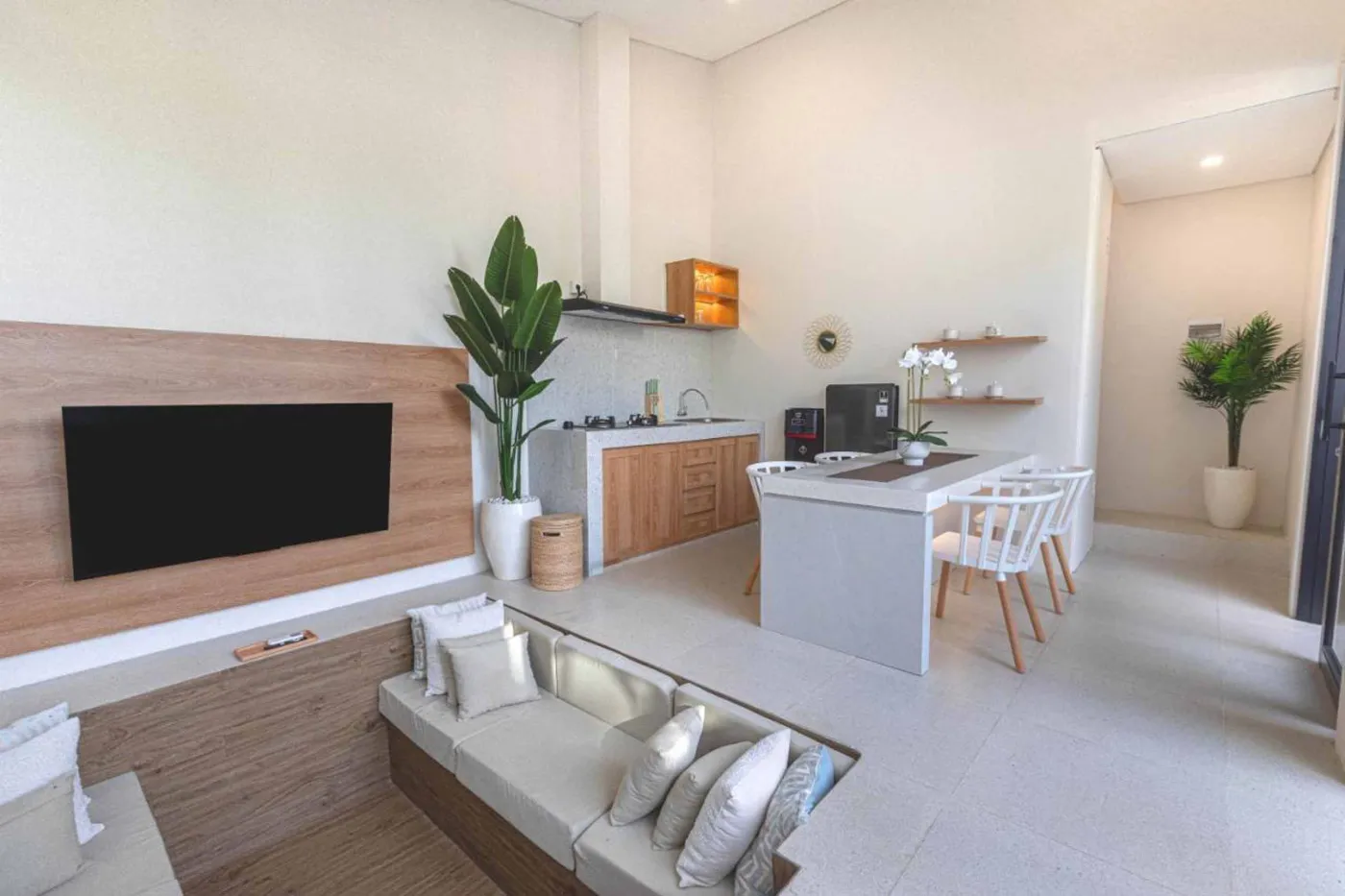 Modern minimalist kitchen with wooden cabinets, white orchids on a central table, fridge, and sink. - Bali Villas