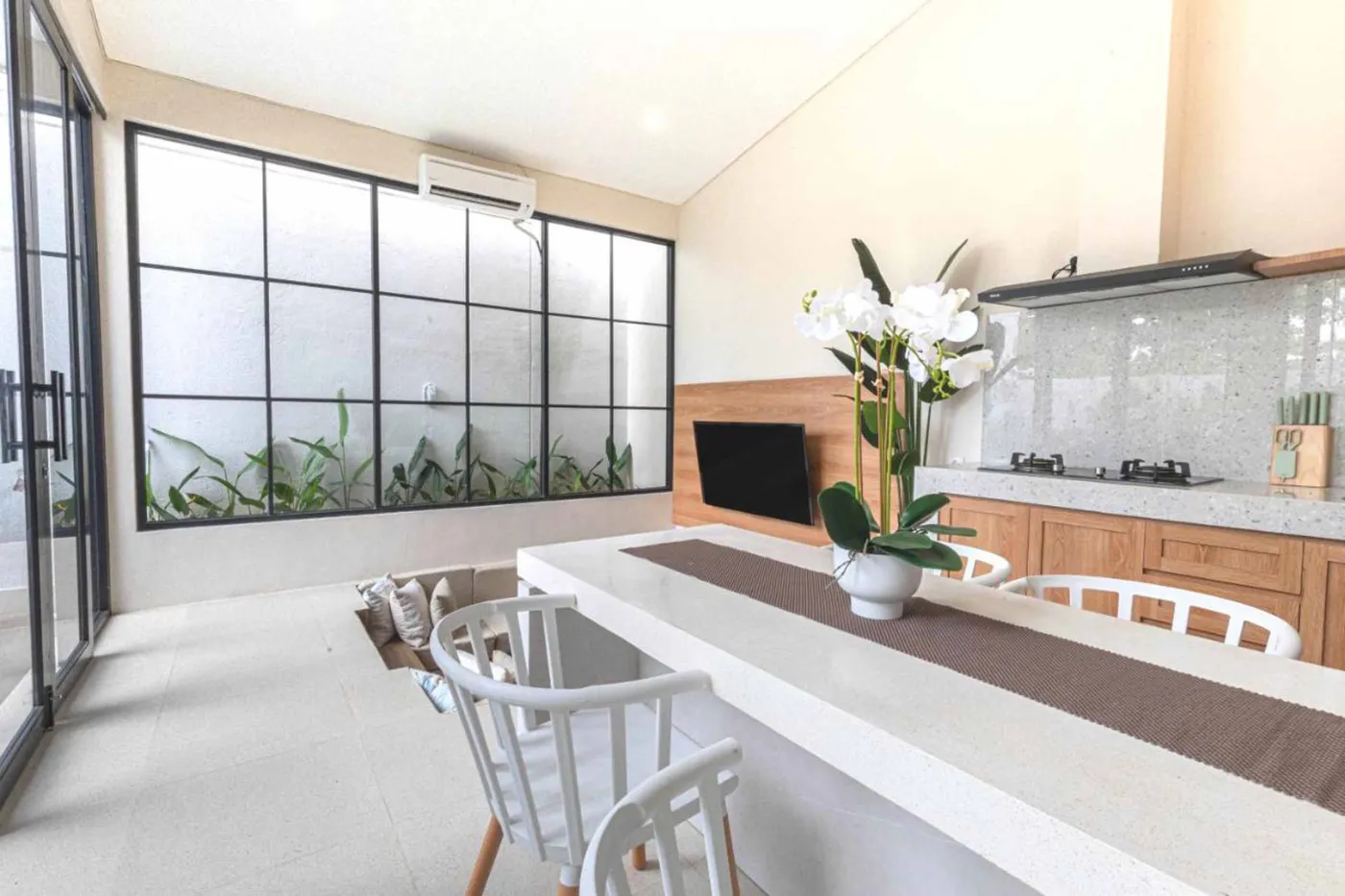 Modern minimalist kitchen with wooden cabinets, white orchids on a central table, fridge, and sink. - Bali Villas
