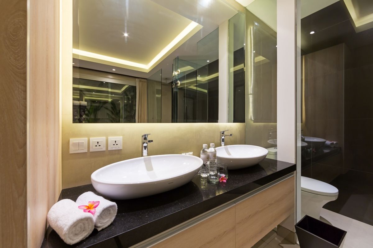 Luxurious Balinese villa terrace at night: wooden table with red petals, white armchairs, tropical banana plants, and sliding glass doors to bedroom. - Bali Villas