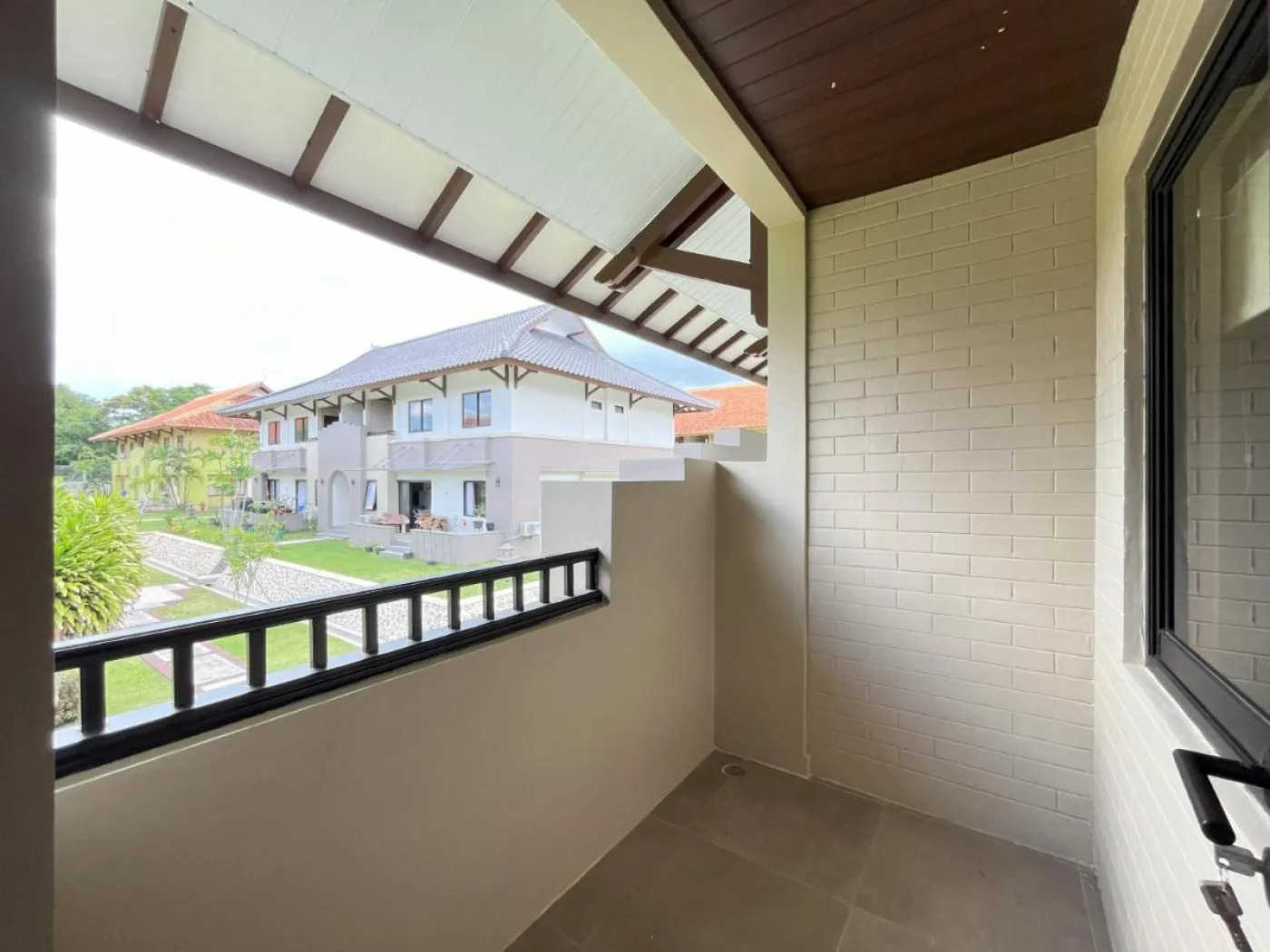 Modern open-plan living room with wooden paneling, white L-shaped sofa, dining table, kitchen cabinets, and large TV in a neutral interior. - Bali Villas