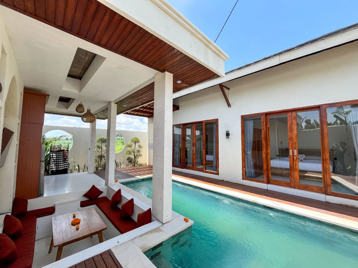 Luxurious Balinese villa with infinity pool, red-cushioned outdoor lounge, and tropical garden views. - Bali Villas
