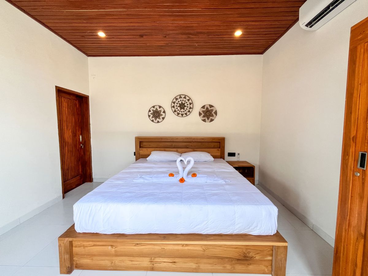 Modern Balinese kitchen with warm teak cabinets, white marble counters, stainless steel appliances, and open archway to outdoor patio with plants and seating. - Bali Villas