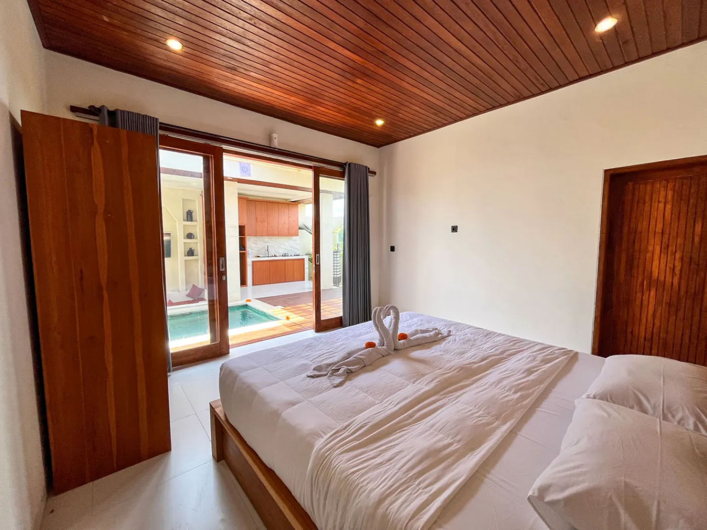 Serene open-air Bali villa lounge with red cushions, wooden table of tropical flowers, and turquoise private pool amid lush plants. - Bali Villas