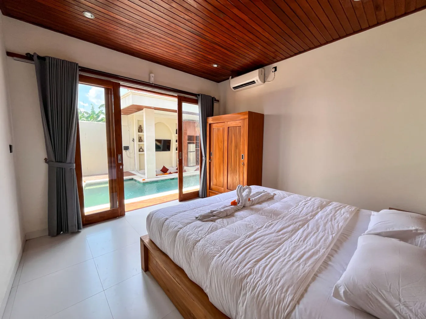 Serene open-air Bali villa lounge with red cushions, wooden table of tropical flowers, and turquoise private pool amid lush plants. - Bali Villas