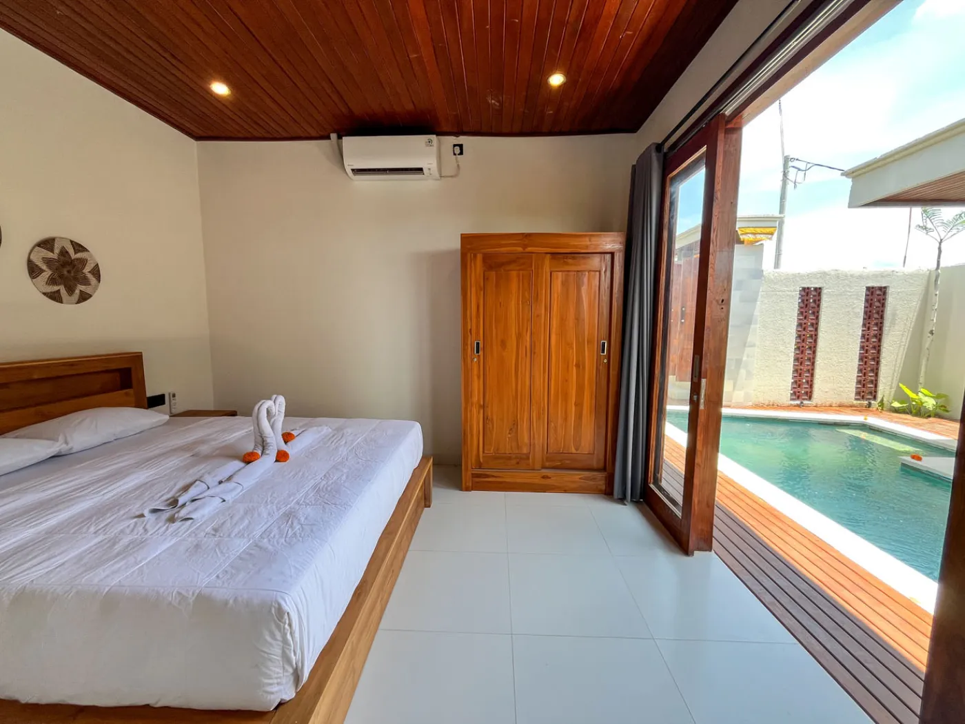 Serene open-air Bali villa lounge with red cushions, wooden table of tropical flowers, and turquoise private pool amid lush plants. - Bali Villas