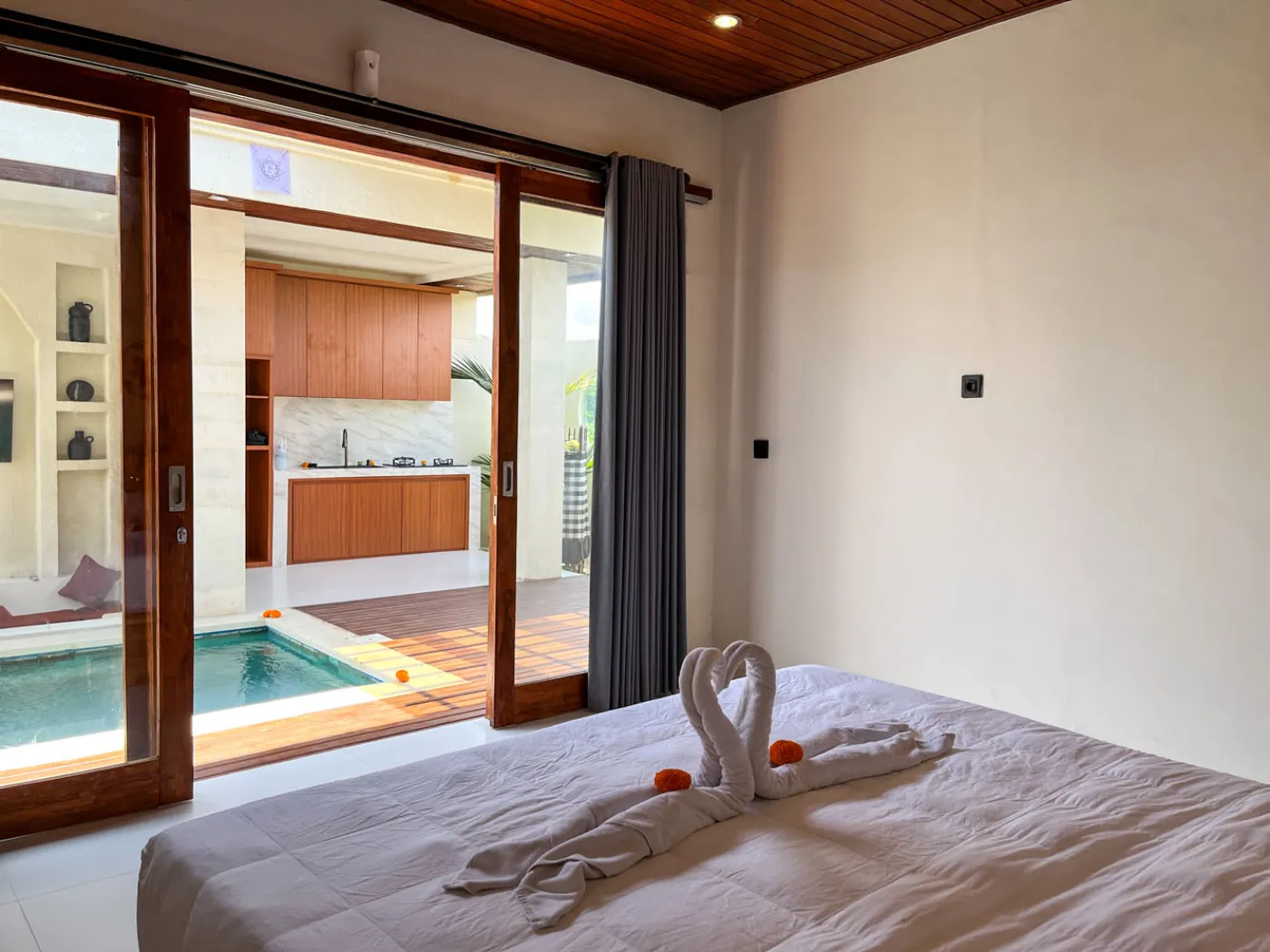 Serene open-air Bali villa lounge with red cushions, wooden table of tropical flowers, and turquoise private pool amid lush plants. - Bali Villas