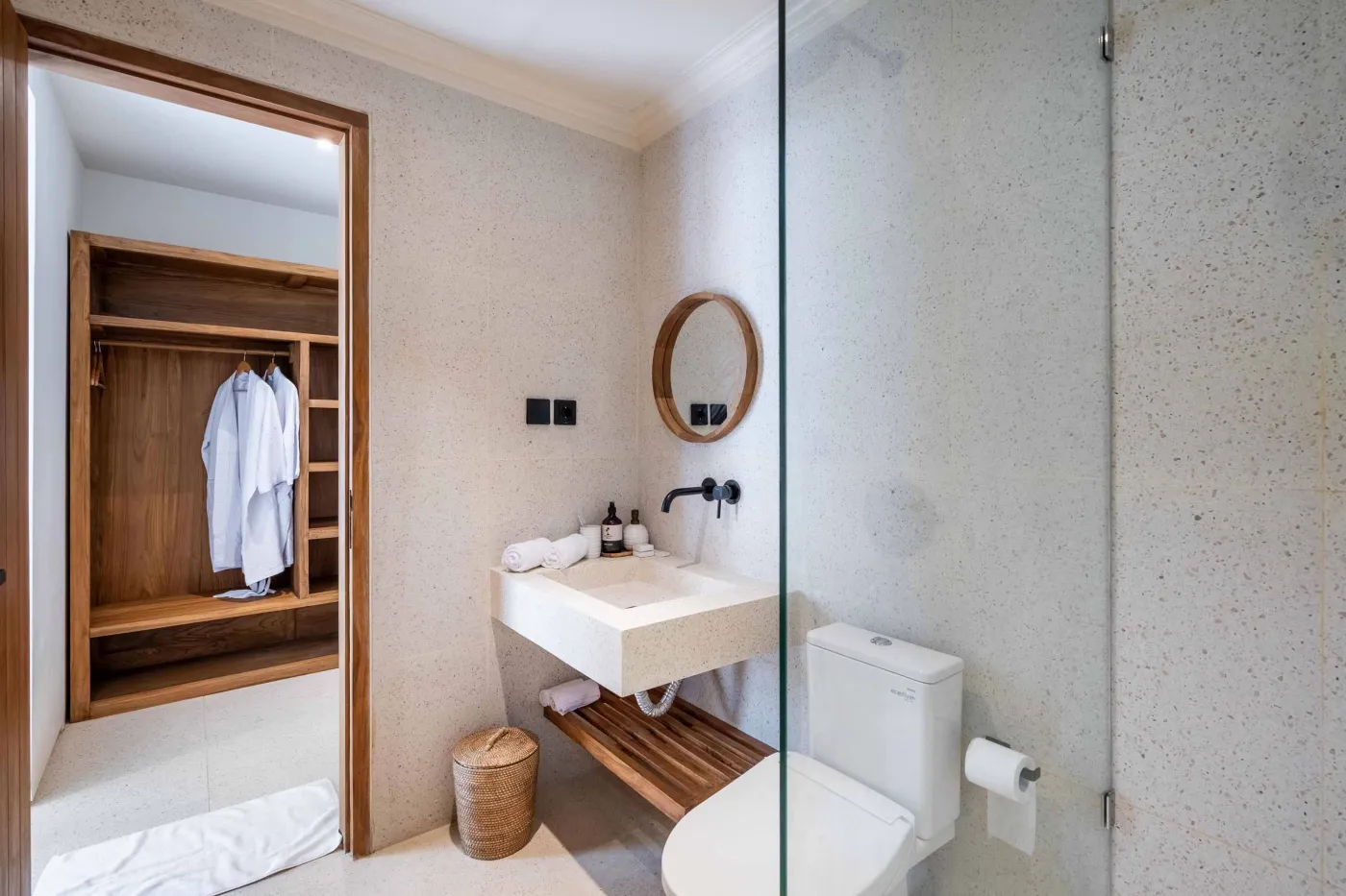 Modern minimalist bathroom with white freestanding bathtub, black rainfall showerhead, and sleek wall niche holding toiletries. - Bali Villas
