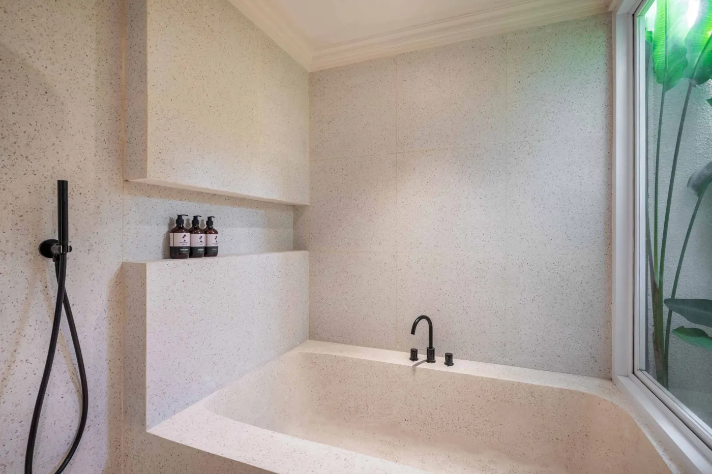 Modern minimalist bathroom with white freestanding bathtub, black rainfall showerhead, and sleek wall niche holding toiletries. - Bali Villas