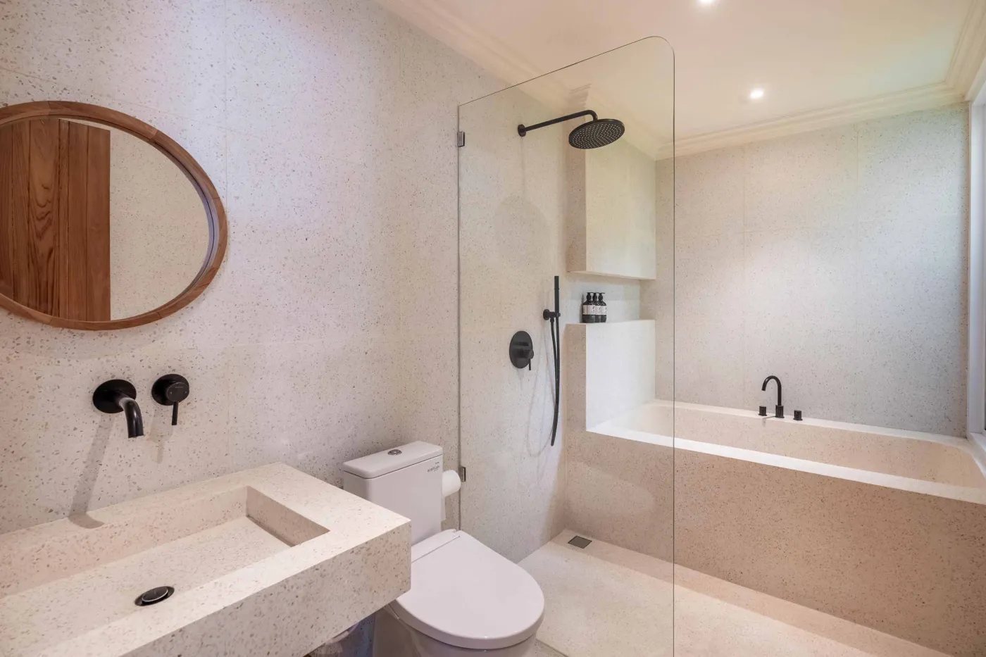 Modern minimalist bathroom with white freestanding bathtub, black rainfall showerhead, and sleek wall niche holding toiletries. - Bali Villas
