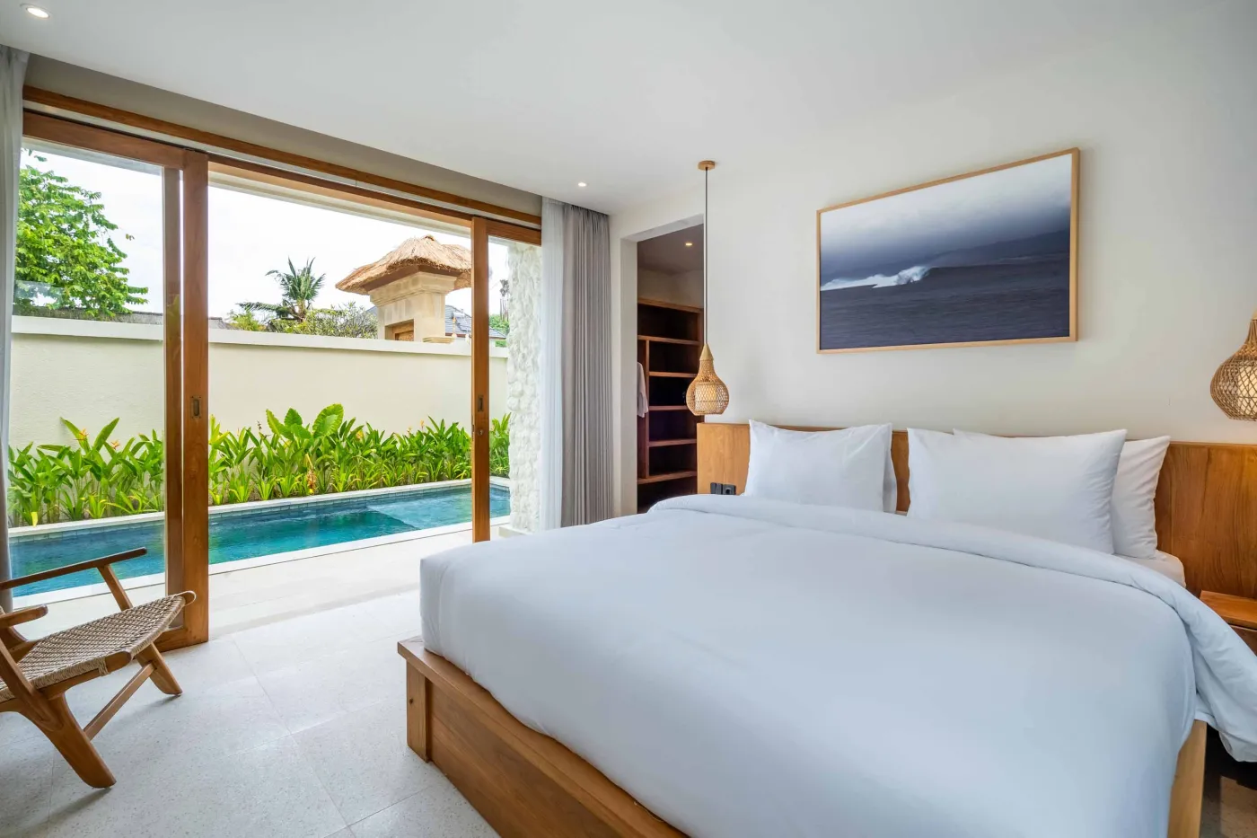 Modern minimalist bathroom with white freestanding bathtub, black rainfall showerhead, and sleek wall niche holding toiletries. - Bali Villas