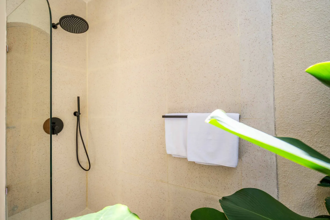 Luxurious tropical bathroom with white freestanding bathtub, rainfall shower, lush green plants, and textured stone walls. - Bali Villas