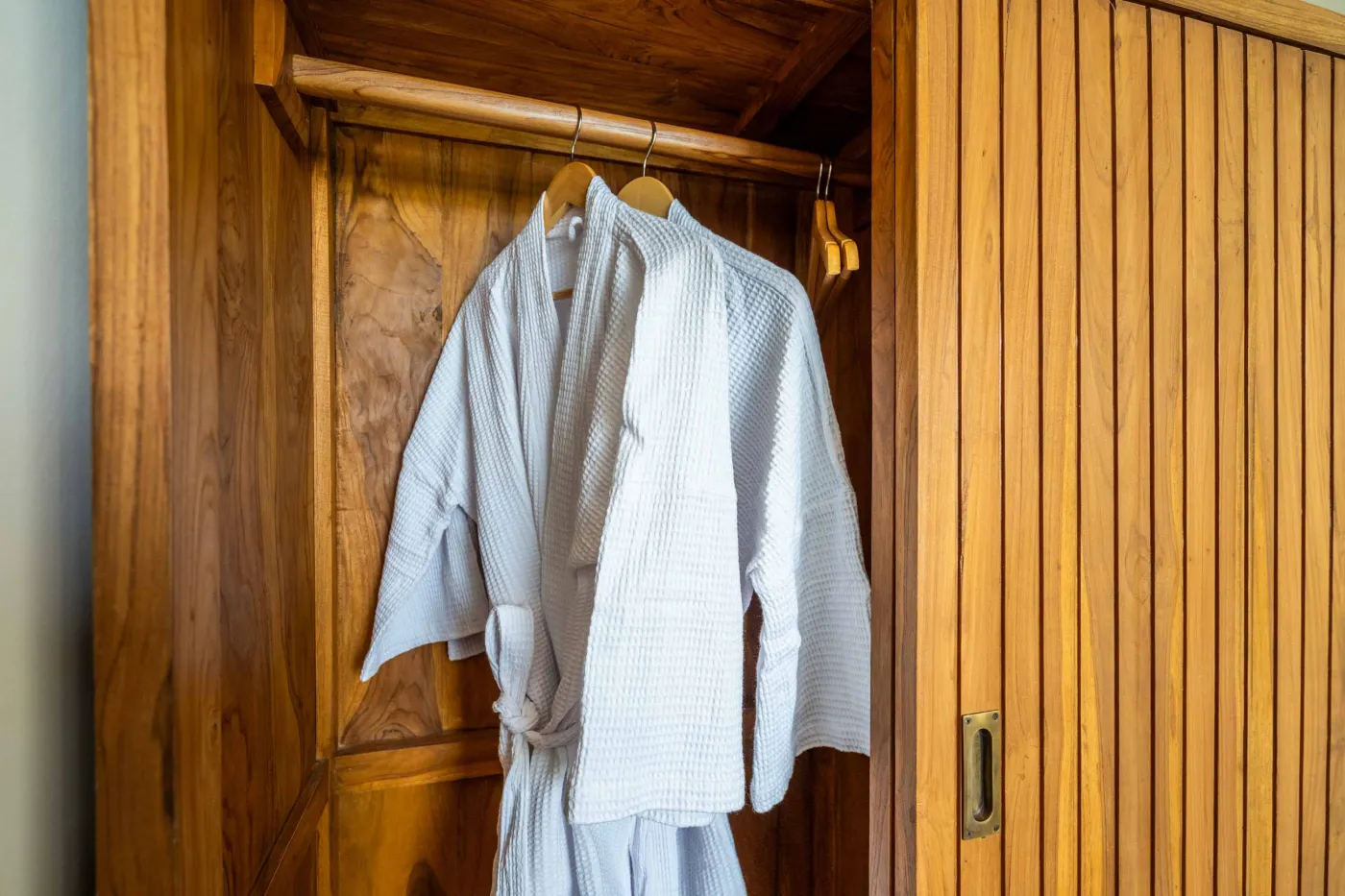 Luxurious tropical bathroom with white freestanding bathtub, rainfall shower, lush green plants, and textured stone walls. - Bali Villas