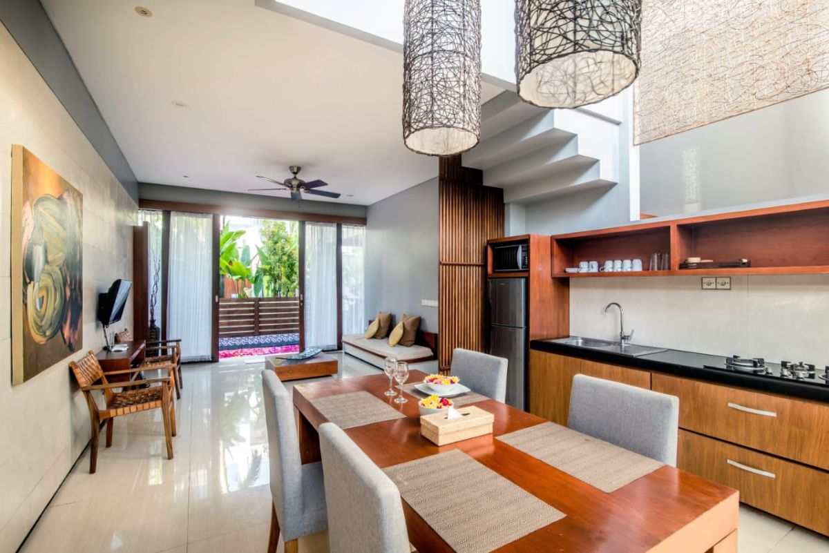 Modern luxury bedroom with king-sized bed, abstract yellow-green wall art, bedside lamps, beige curtains, and woven bench on wooden floor. - Bali Villas