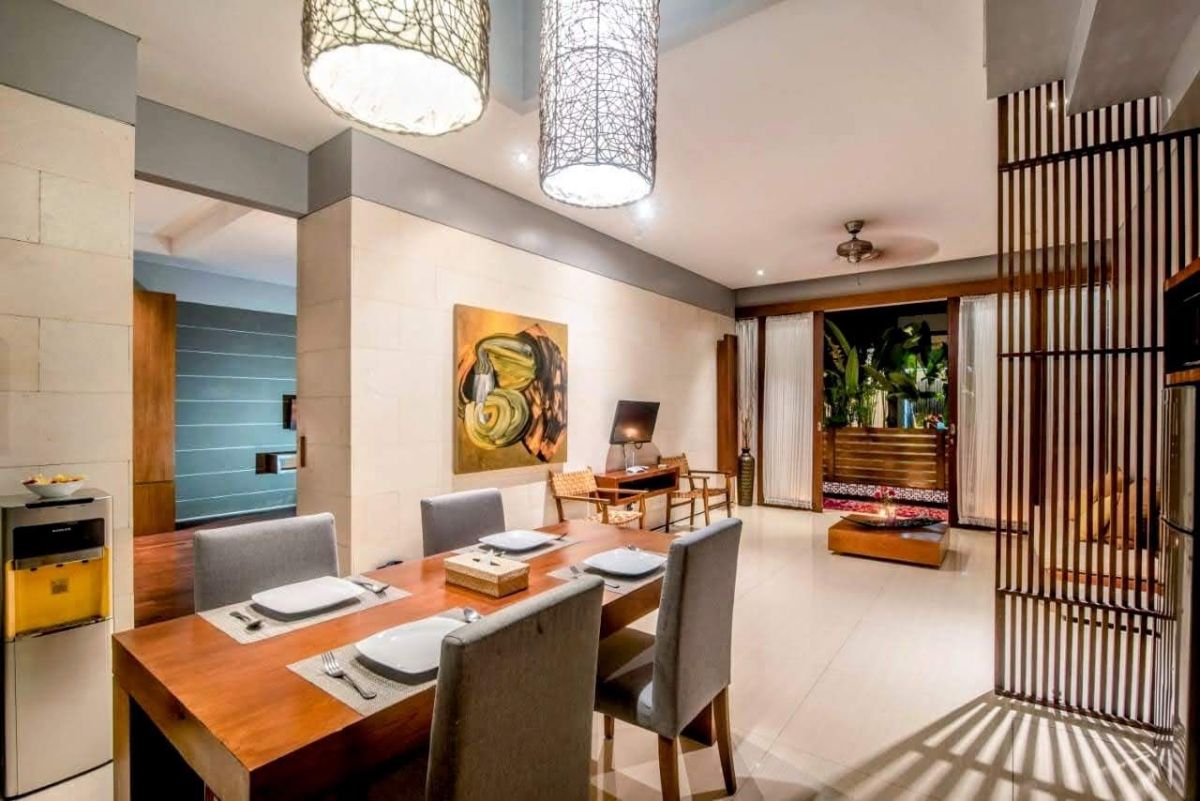 Modern luxury bedroom with king-sized bed, abstract yellow-green wall art, bedside lamps, beige curtains, and woven bench on wooden floor. - Bali Villas