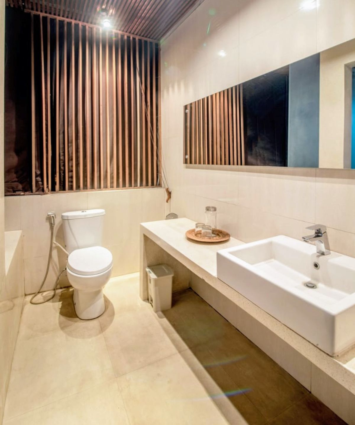 Modern luxury bedroom with king-sized bed, abstract yellow-green wall art, bedside lamps, beige curtains, and woven bench on wooden floor. - Bali Villas