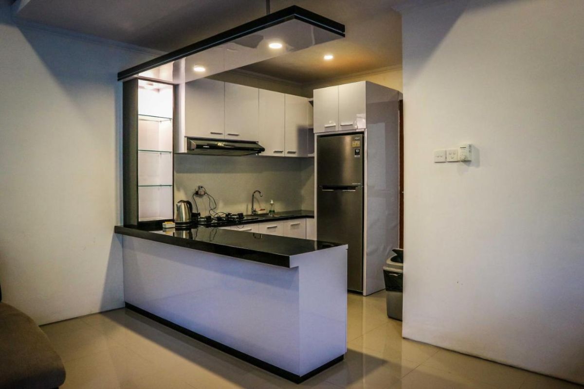 Tropical resort poolside with curved rattan lounge chairs, white umbrella, and lush palm-fringed jungle views. - Bali Villas