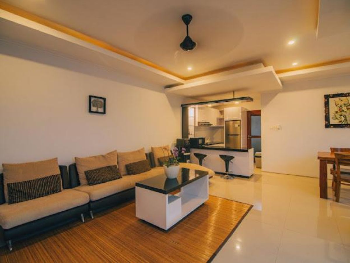 Tropical resort poolside with curved rattan lounge chairs, white umbrella, and lush palm-fringed jungle views. - Bali Villas