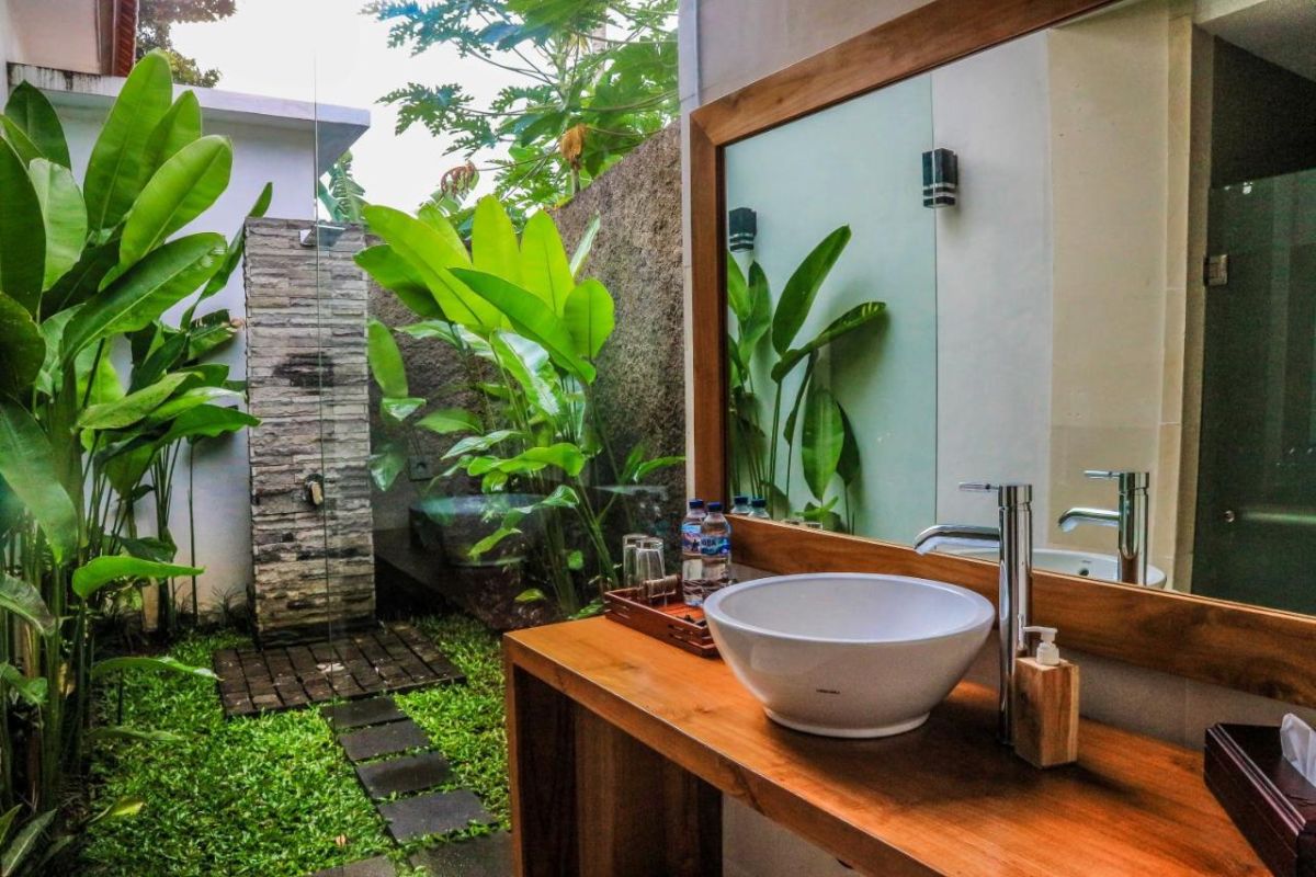 Tropical resort poolside with curved rattan lounge chairs, white umbrella, and lush palm-fringed jungle views. - Bali Villas