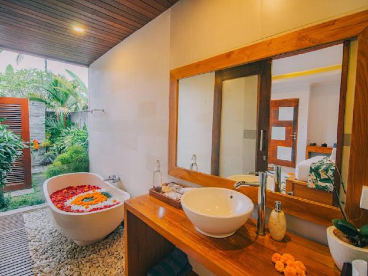 Tropical resort poolside with curved rattan lounge chairs, white umbrella, and lush palm-fringed jungle views. - Bali Villas