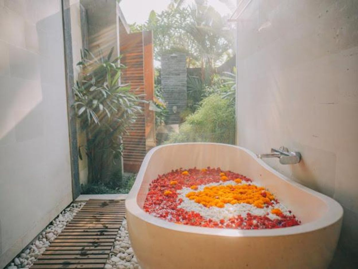 Tropical resort poolside with curved rattan lounge chairs, white umbrella, and lush palm-fringed jungle views. - Bali Villas