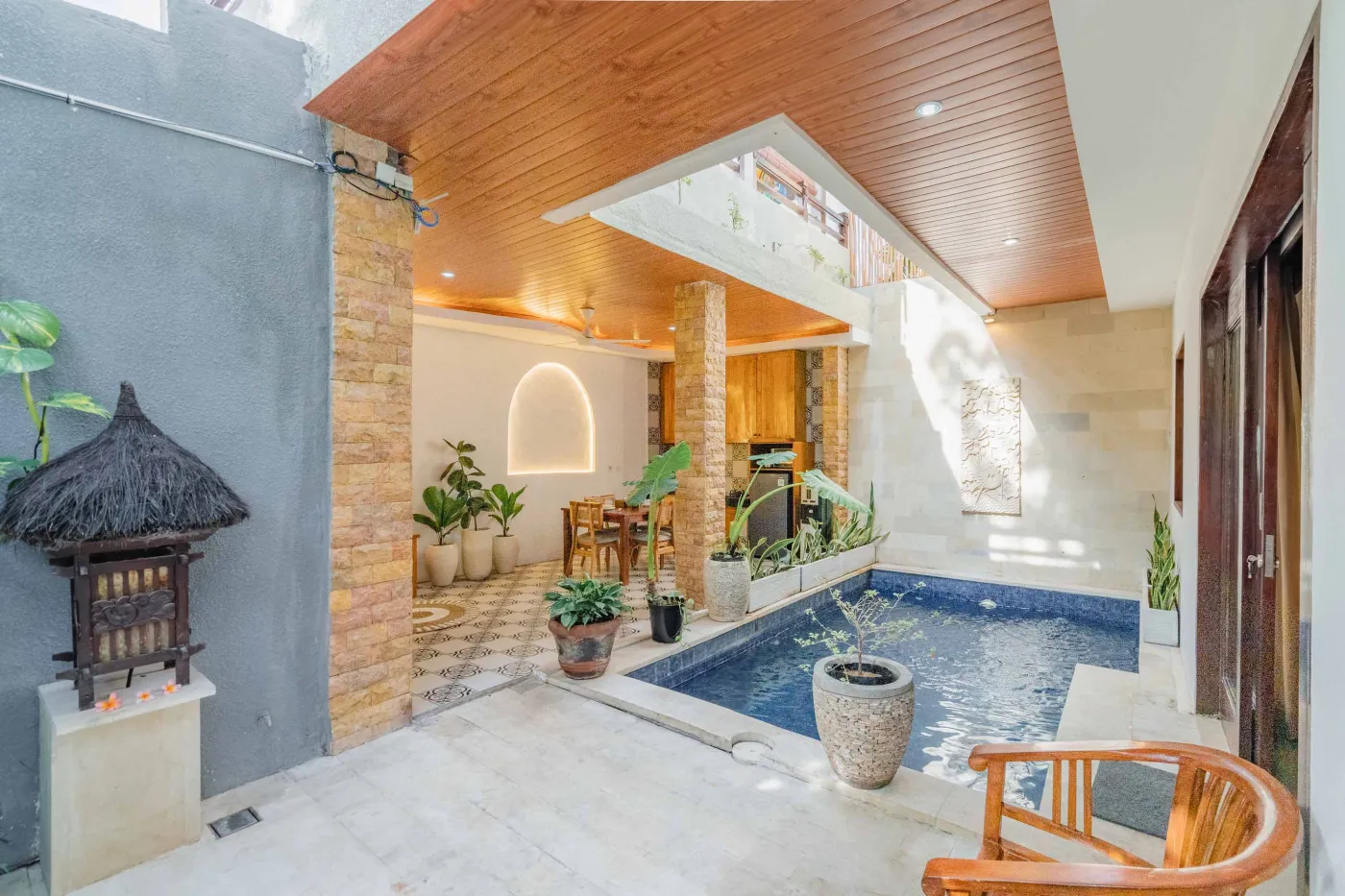 Balinese kitchen with wooden cabinets, checkered tiled backsplash, and dining table overlooking a private pool. - Bali Villas