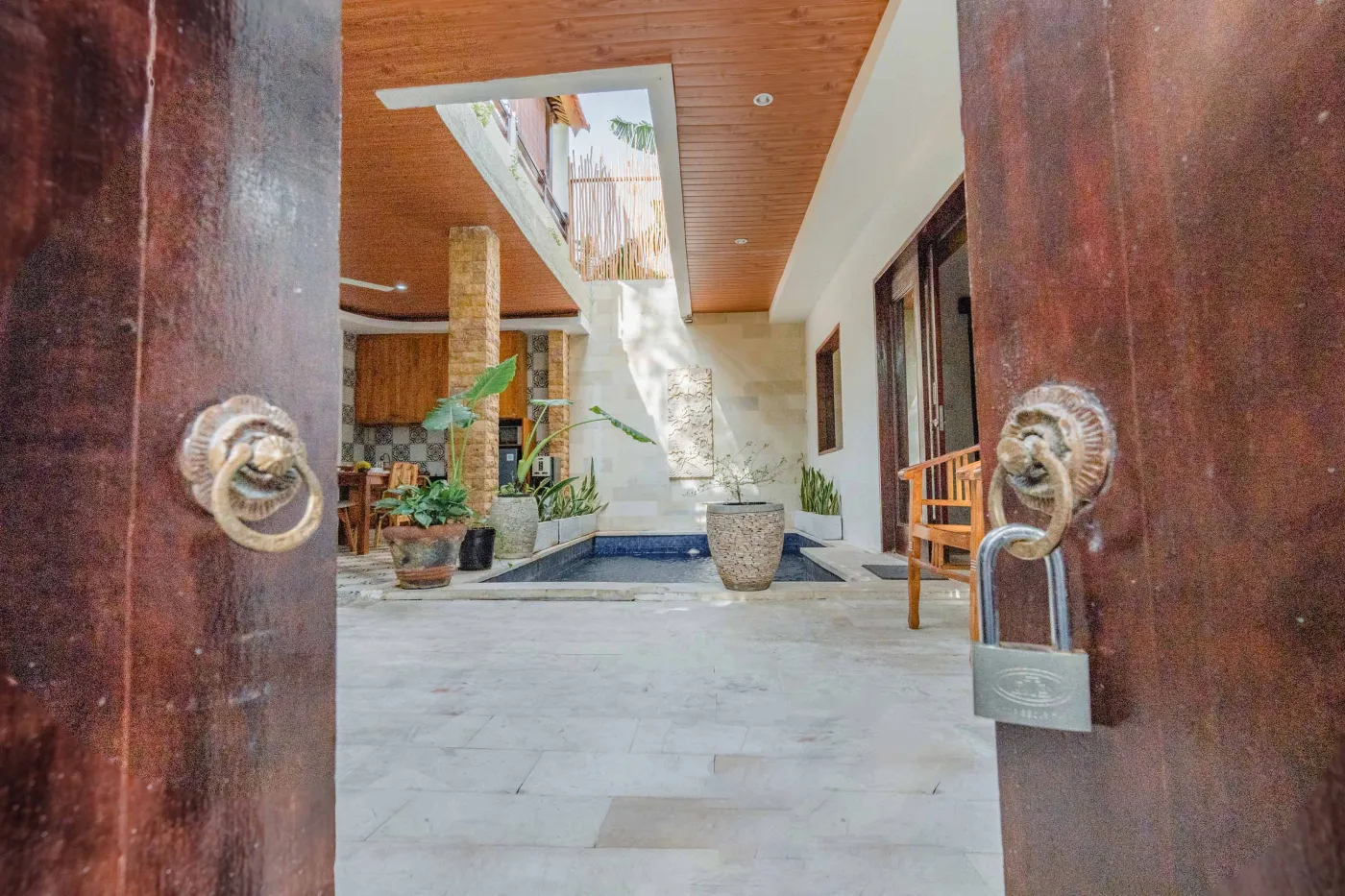 Balinese kitchen with wooden cabinets, checkered tiled backsplash, and dining table overlooking a private pool. - Bali Villas