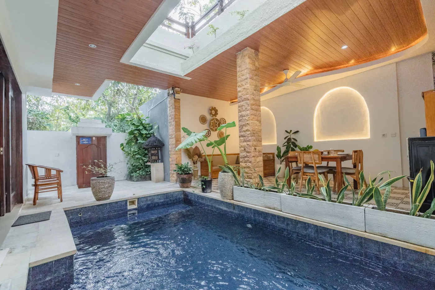 Balinese kitchen with wooden cabinets, checkered tiled backsplash, and dining table overlooking a private pool. - Bali Villas