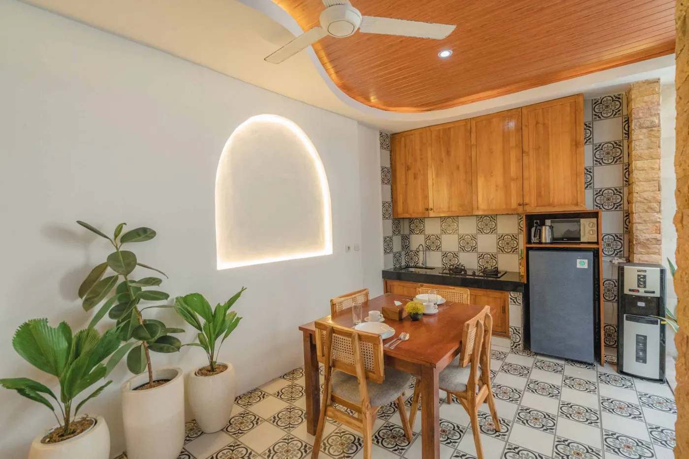 Balinese kitchen with wooden cabinets, checkered tiled backsplash, and dining table overlooking a private pool. - Bali Villas