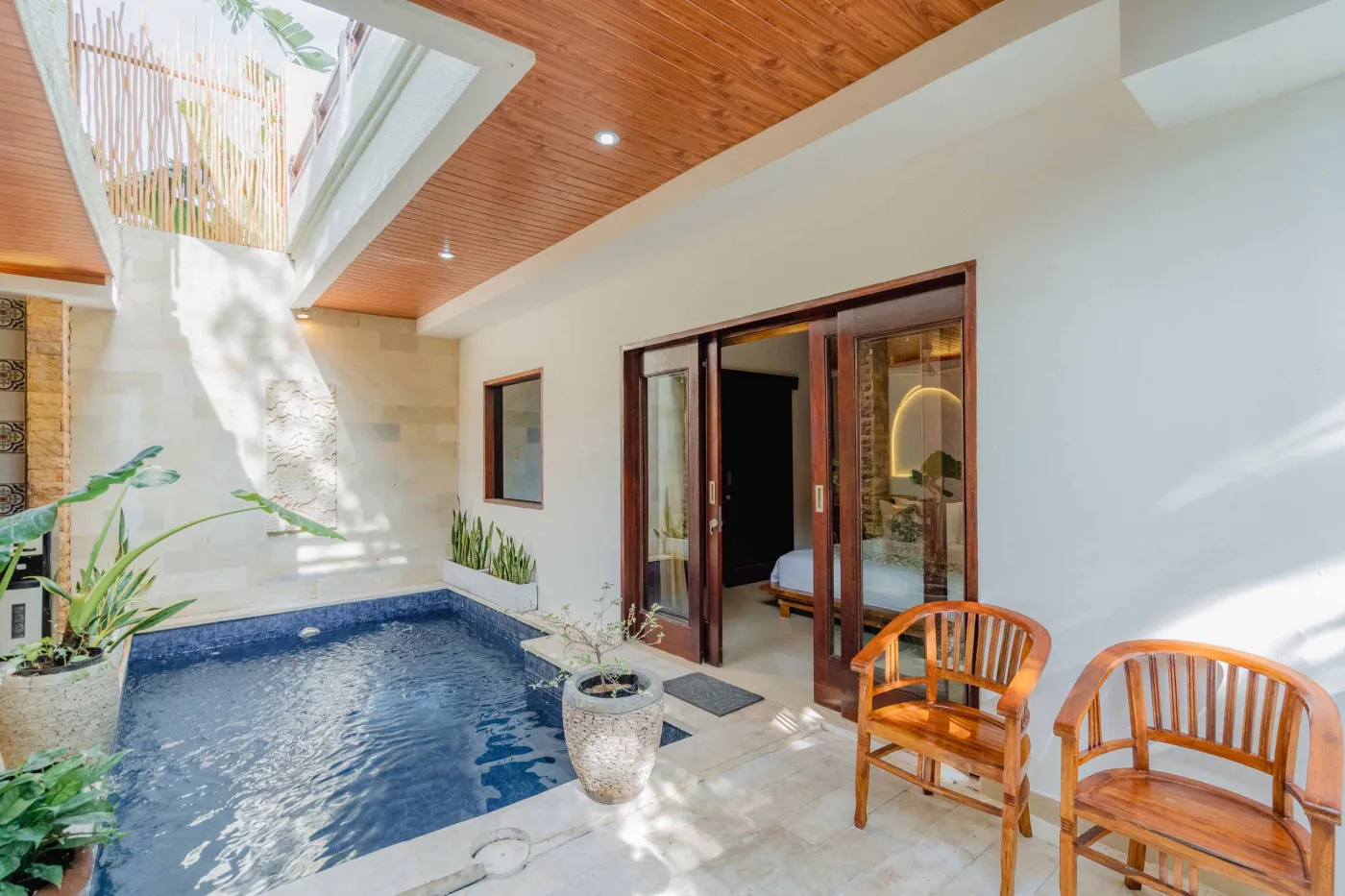 Balinese kitchen with wooden cabinets, checkered tiled backsplash, and dining table overlooking a private pool. - Bali Villas