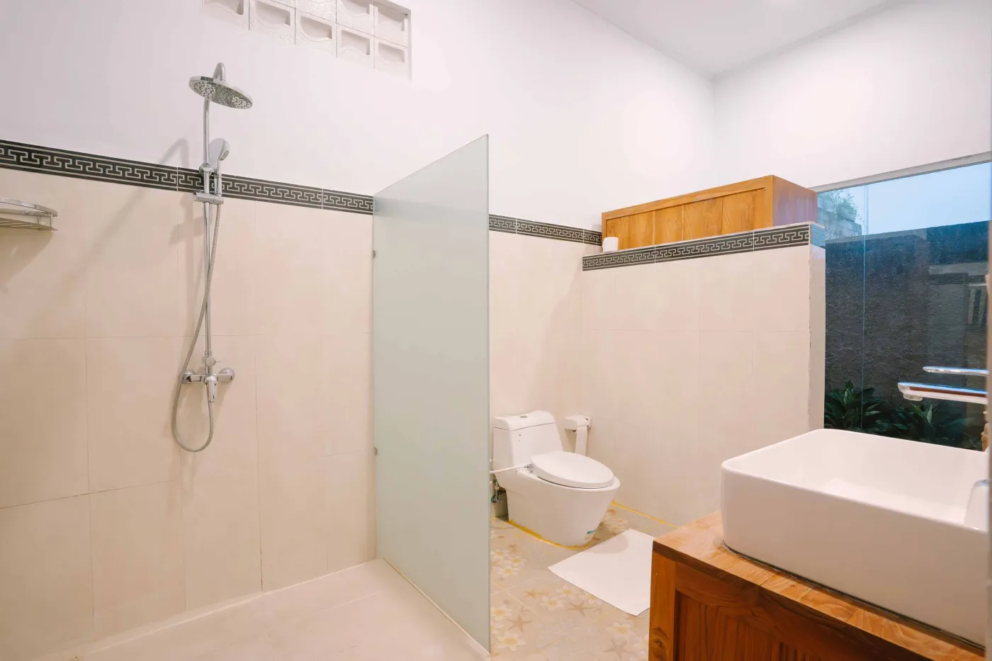 Spacious modern bathroom with white vanity, ornate mirror, toilet, and tropical garden view through frosted glass door. - Bali Villas
