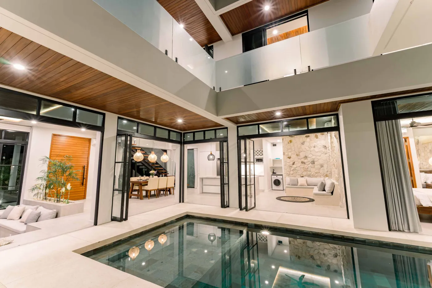 Luxurious modern bathroom featuring a white freestanding bathtub filled with water and red rose petals, adjacent glass shower, large window, and potted plant. - Bali Villas
