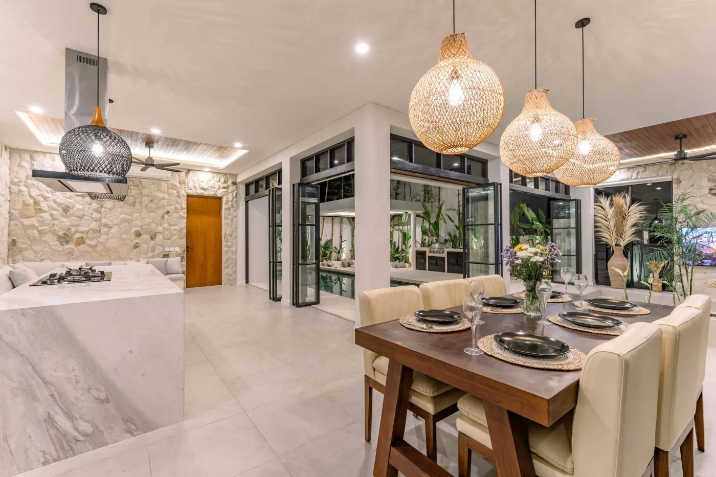 Luxurious modern bathroom featuring a white freestanding bathtub filled with water and red rose petals, adjacent glass shower, large window, and potted plant. - Bali Villas