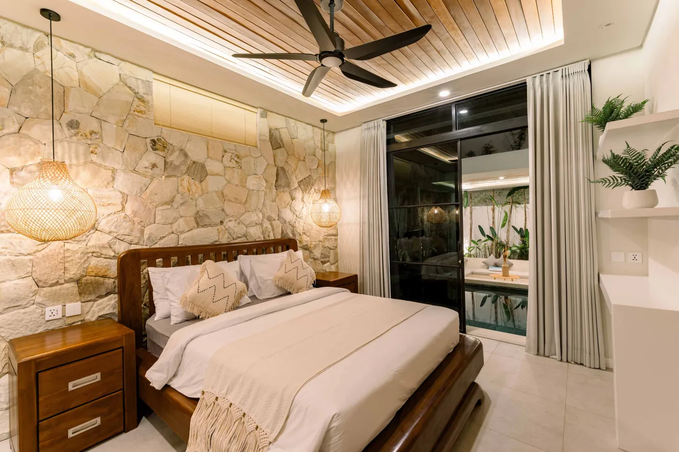 Luxurious modern bathroom featuring a white freestanding bathtub filled with water and red rose petals, adjacent glass shower, large window, and potted plant. - Bali Villas